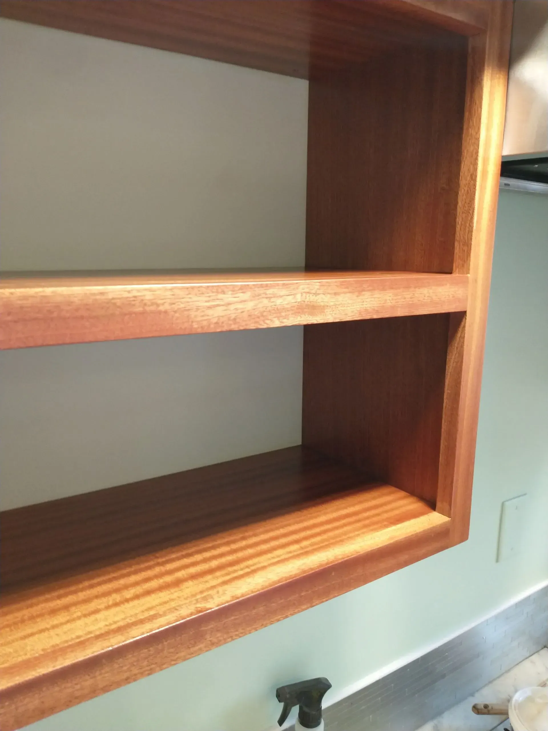 Wooden shelving unit with two shelves, mounted on a light green wall, over a countertop.