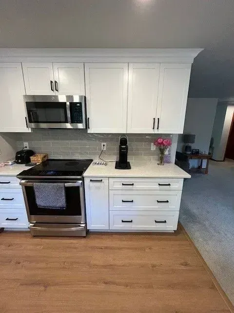 White kitchen with stainless steel appliances, white cabinets, and light wood floors.