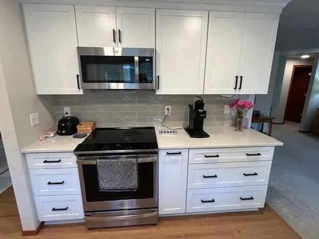 White kitchen cabinets with stainless steel appliances, countertop, and coffee maker.