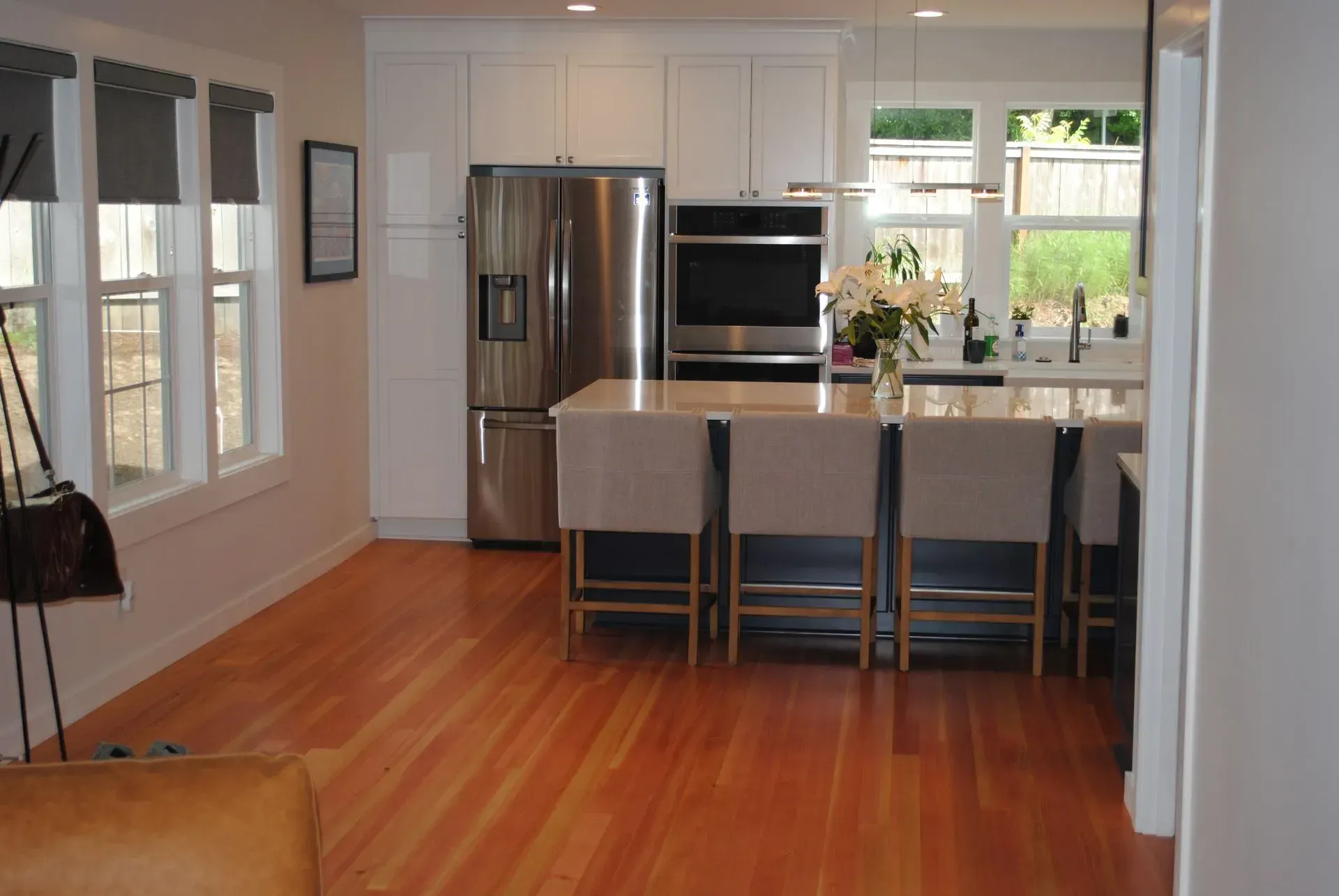 Modern kitchen with stainless steel appliances, white cabinets, island with stools, and hardwood floors.