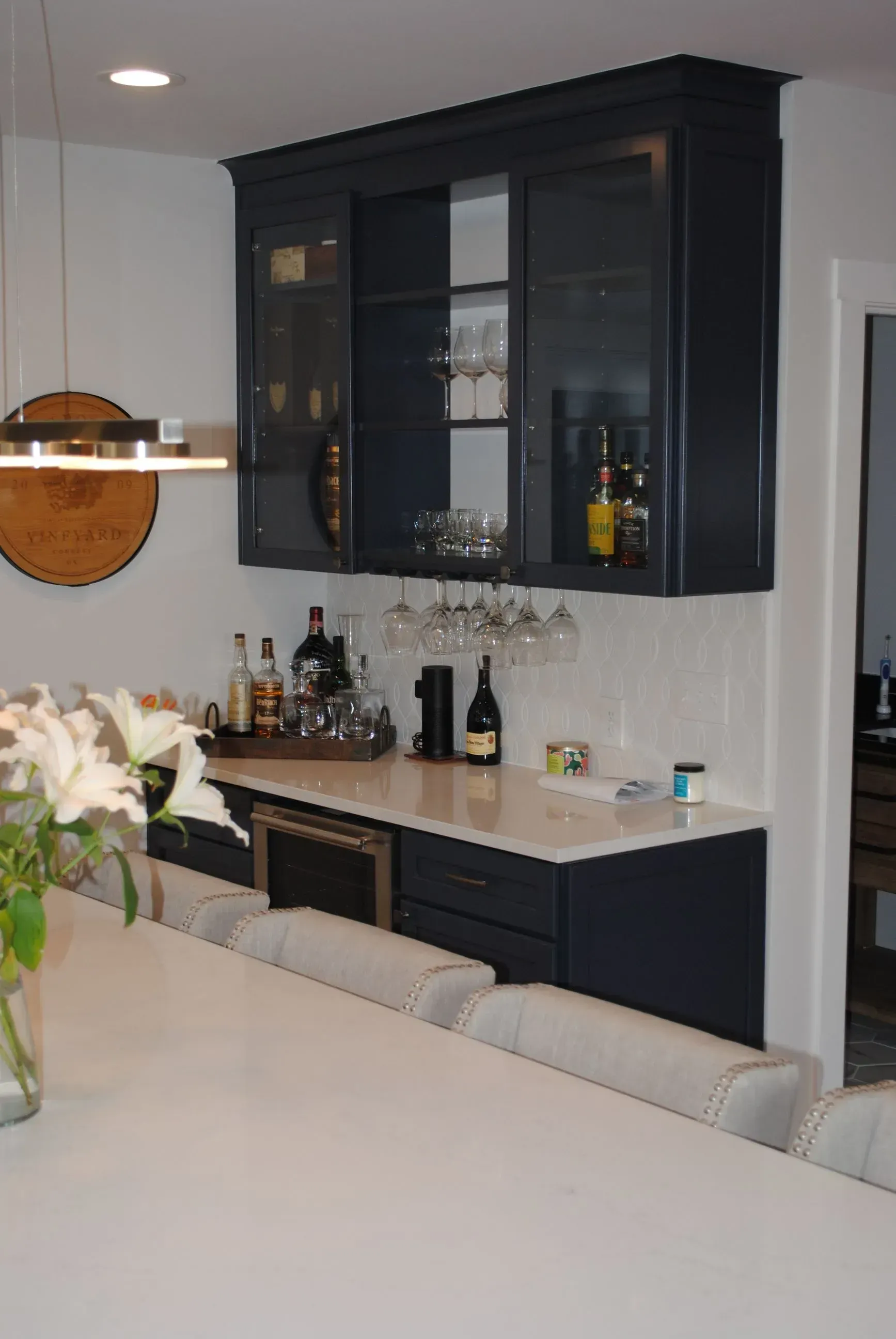 Dark blue built-in bar with glass-front cabinets, bottles, wine glasses, and a small refrigerator.