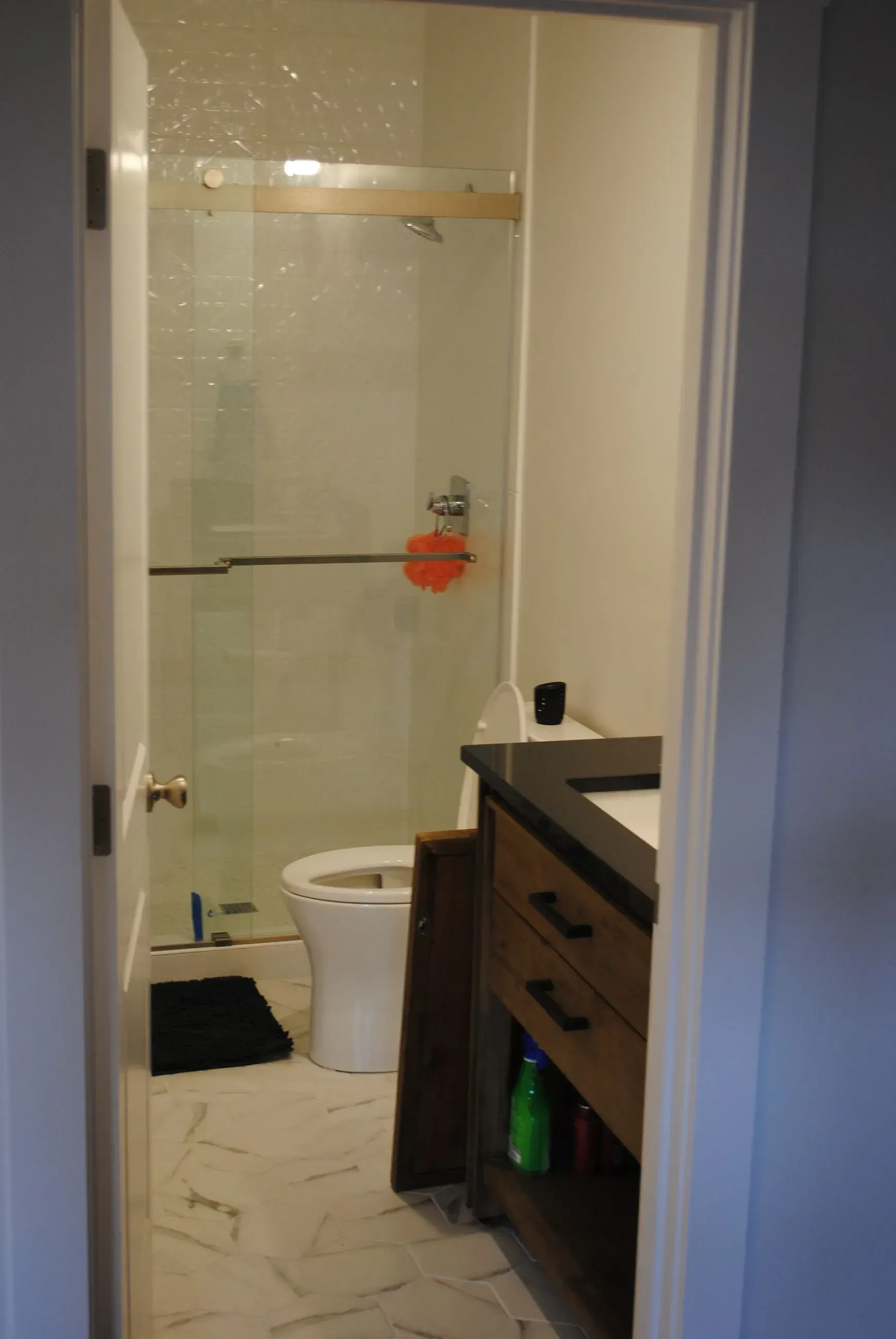 Bathroom interior with a shower, toilet, and vanity, viewed through the doorway. White walls and marble tile floors.