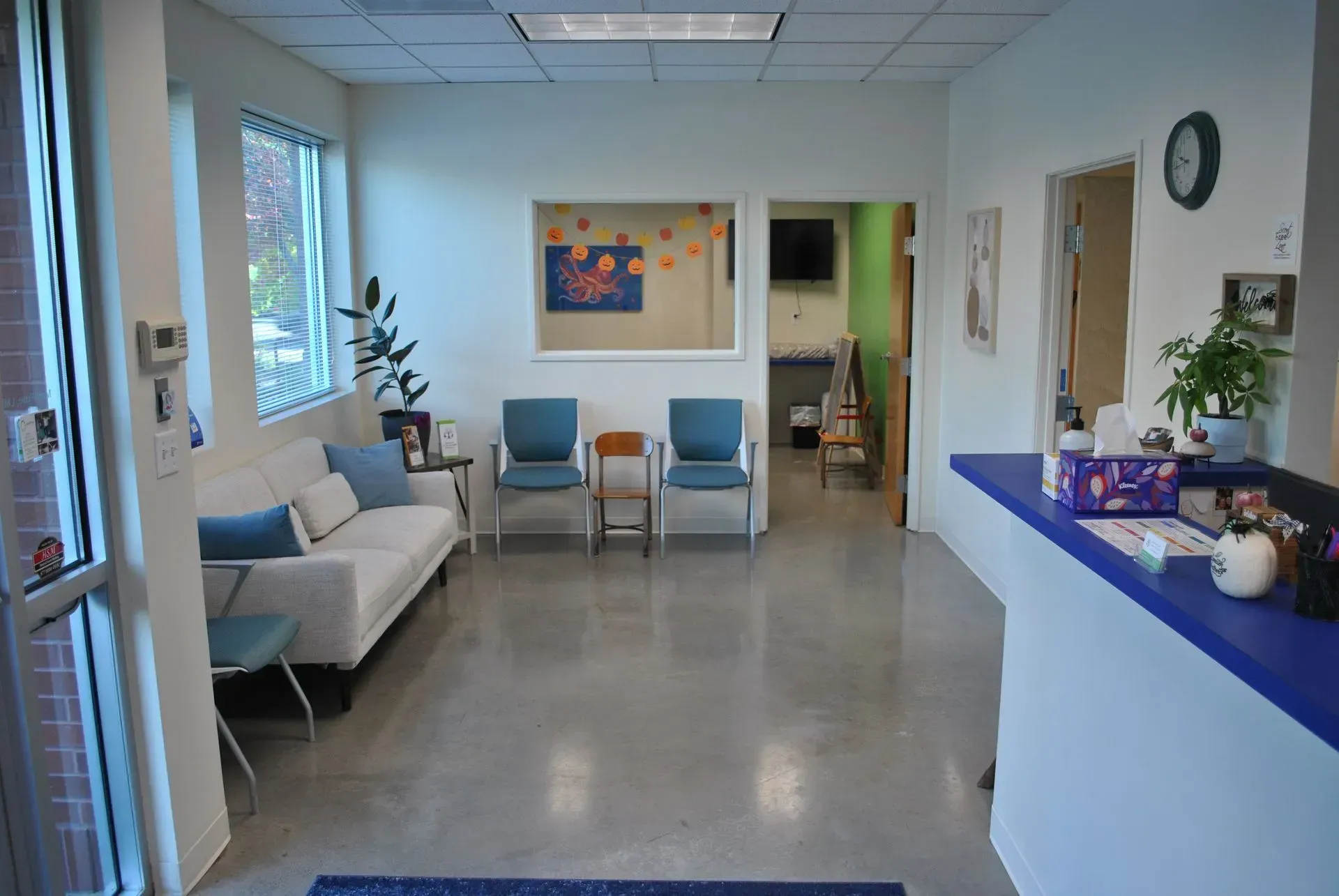 Reception area: White couch, blue chairs, and a blue-topped reception desk. Bright, modern space.