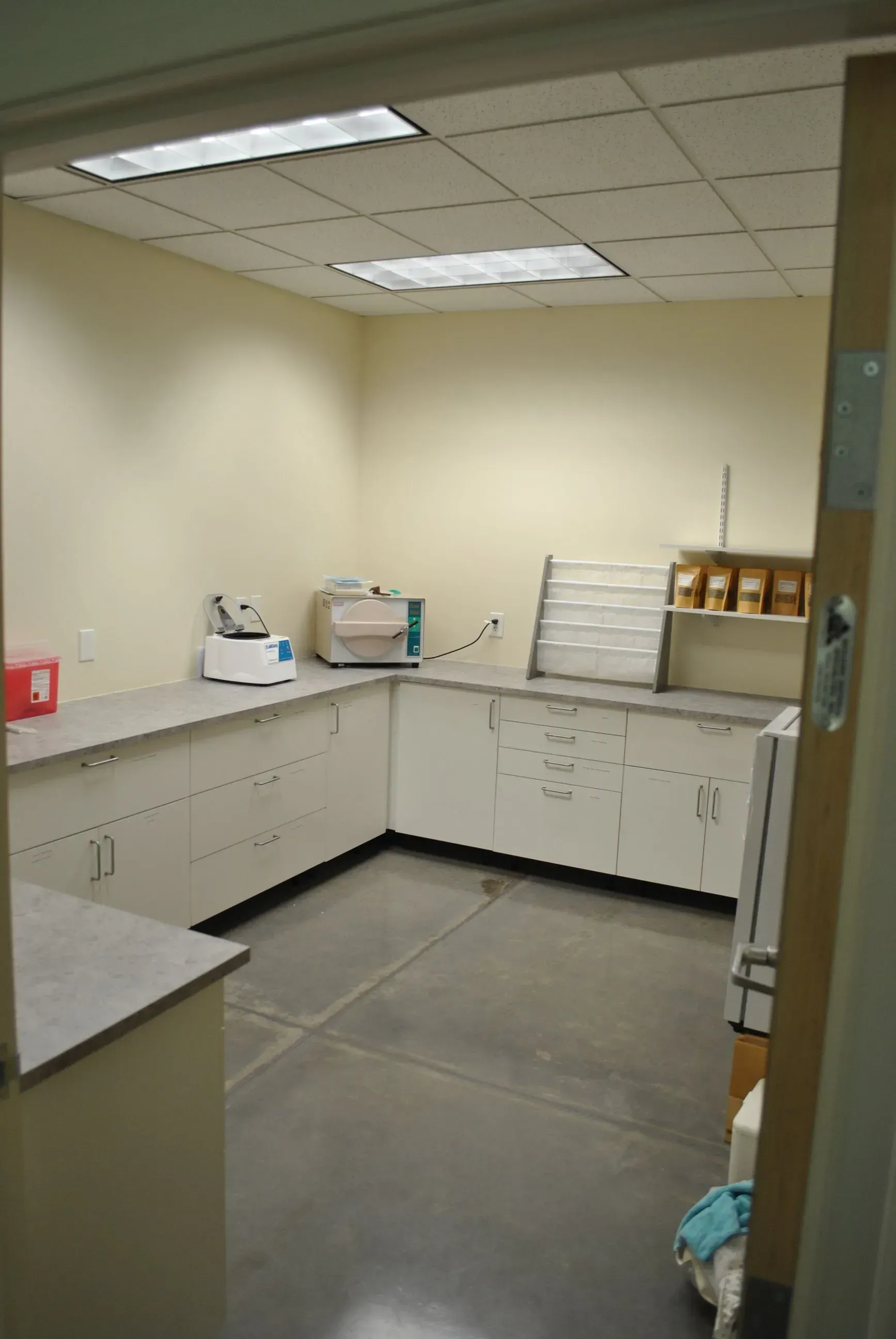 A small lab with white cabinets, a gray countertop, and a sterilizer.