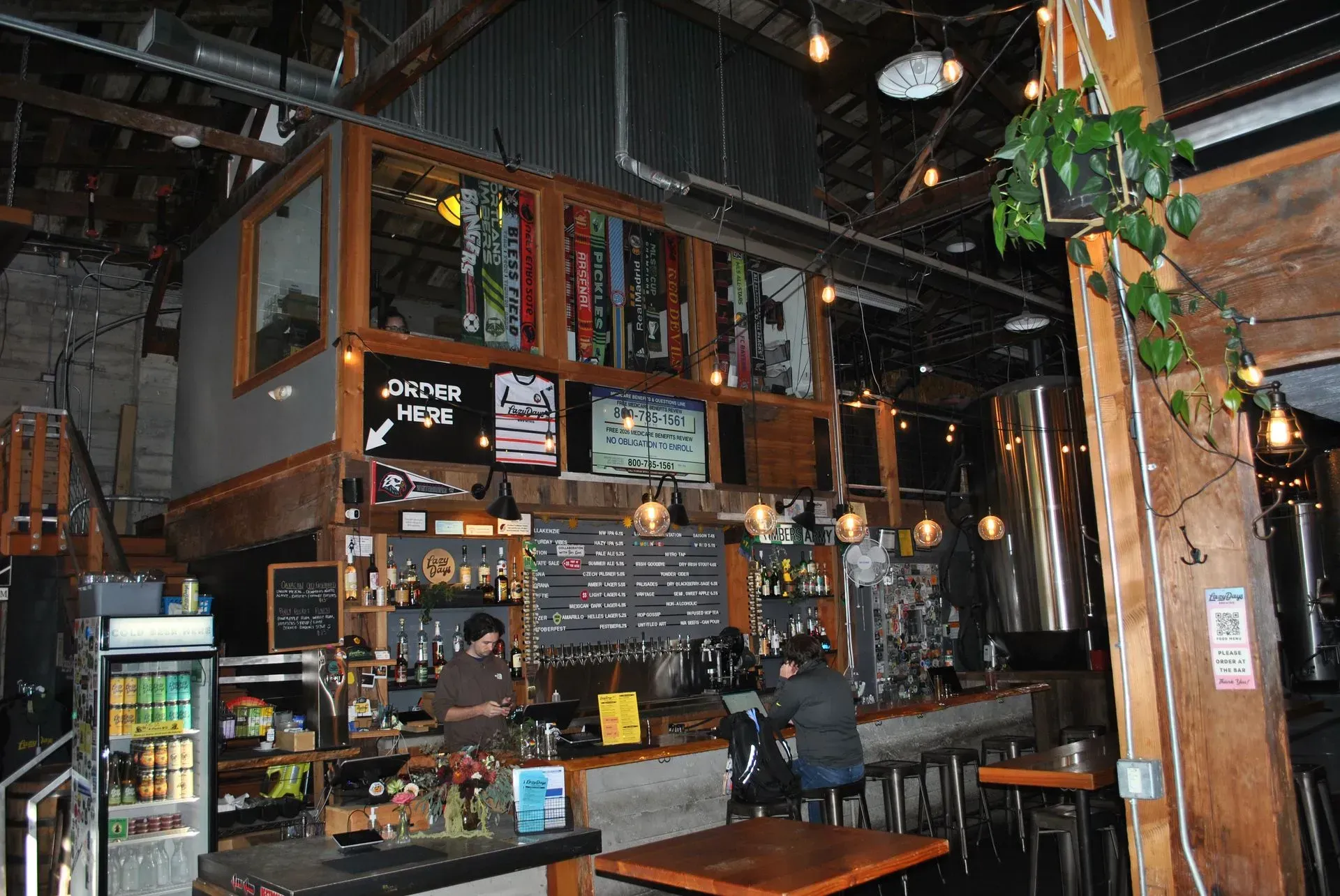 Interior of a bar, wood and metal design. Bartenders behind a bar, patrons seated at barstools.