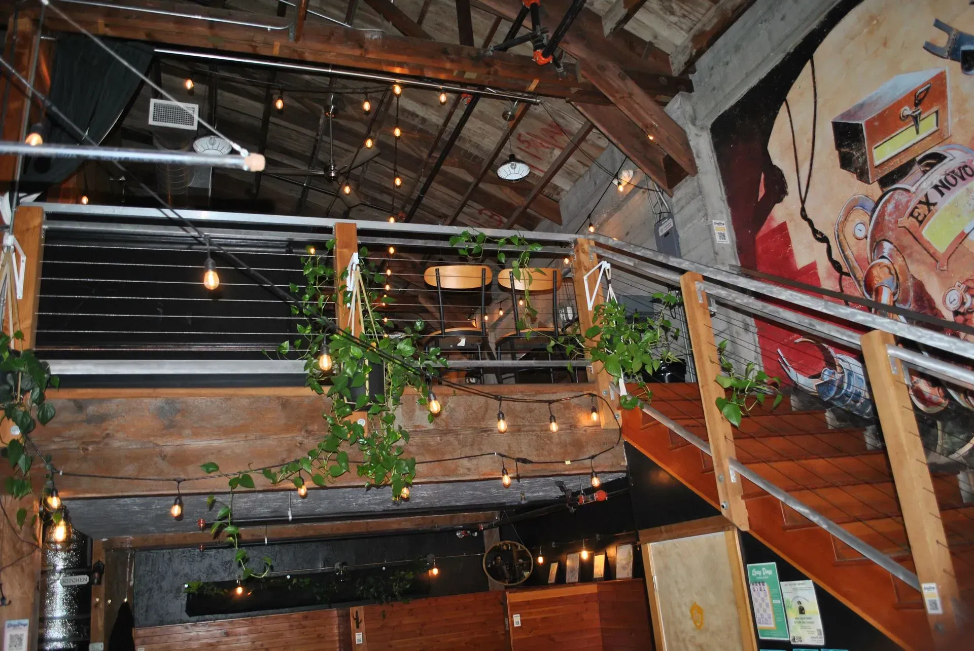 Interior of a bar with a mezzanine, string lights, and a mural.