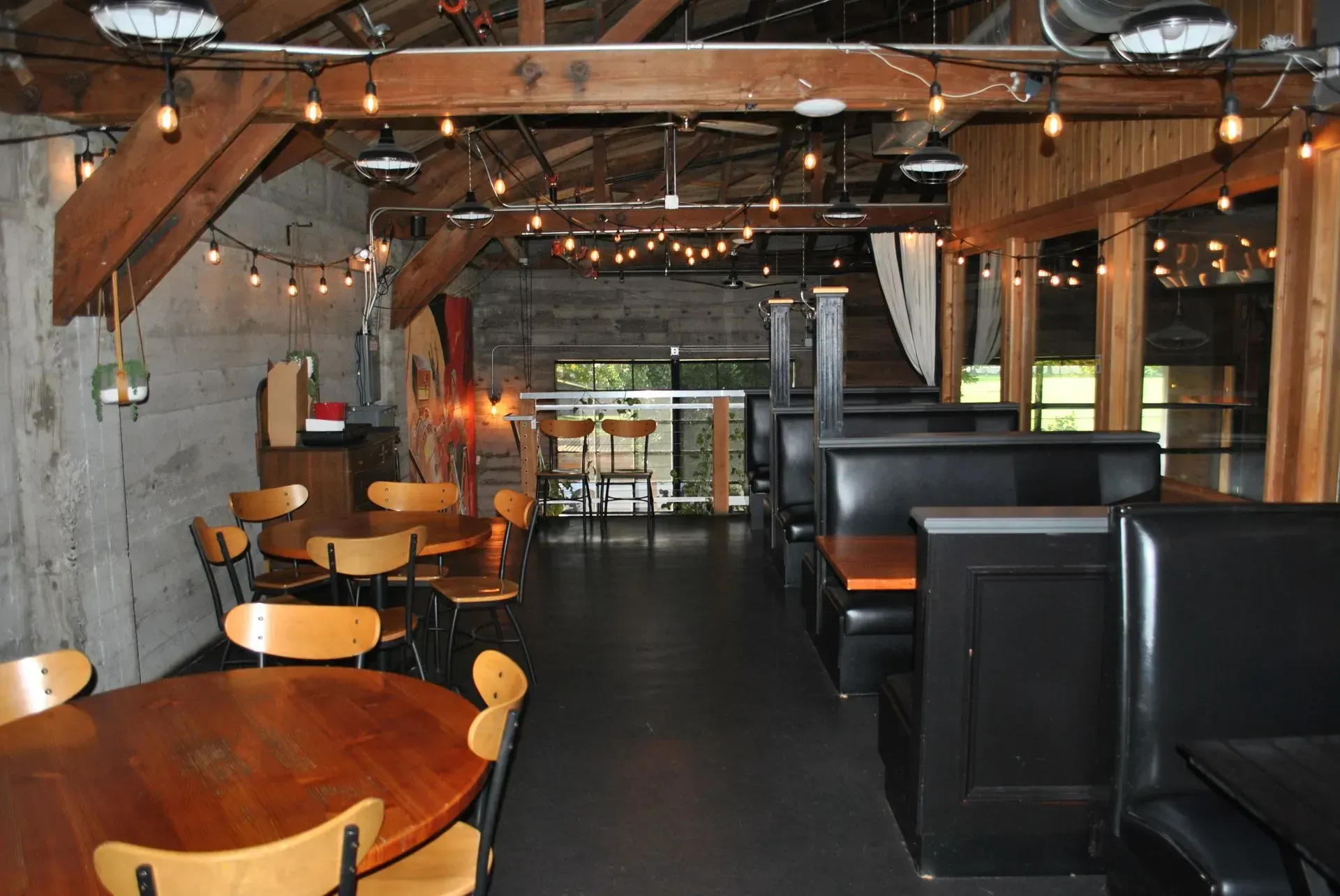 Restaurant interior: wooden tables and chairs, black booths, exposed beams, string lights.