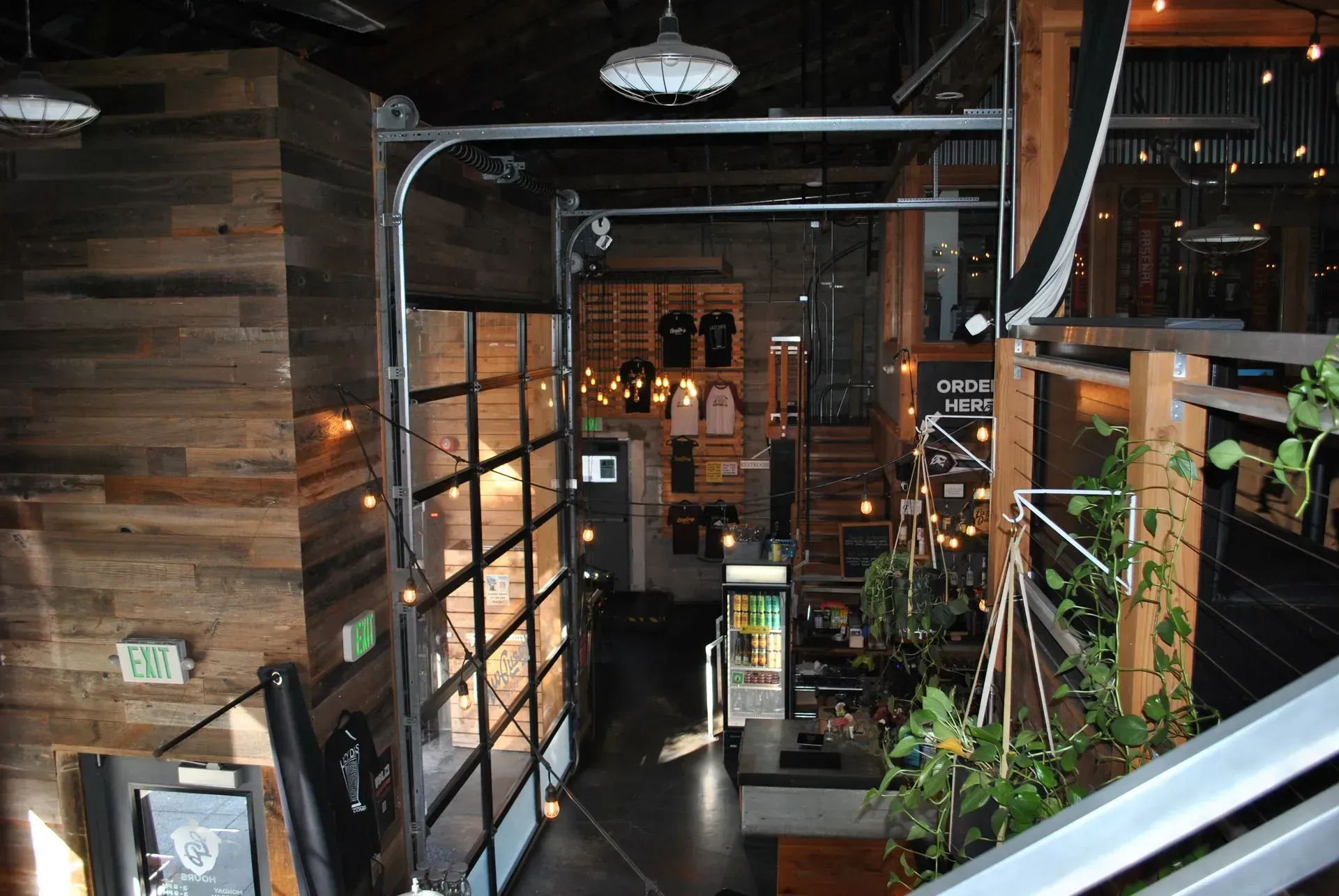 Interior of a modern brewery.  Wood paneling, metal garage door, plants, and a merchandise area are visible.