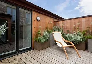 Wooden patio with chair, planters, and wood-paneled walls, next to a sliding glass door.