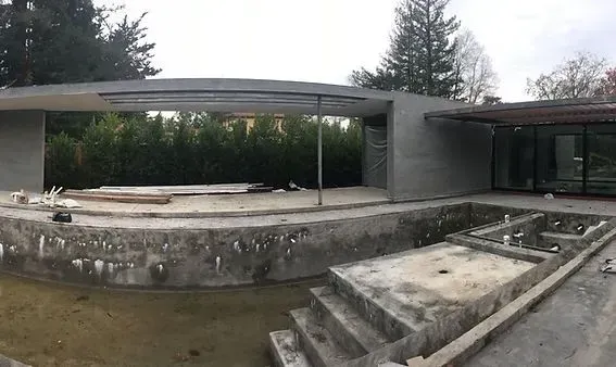 A concrete building exterior with an empty pool and construction materials.
