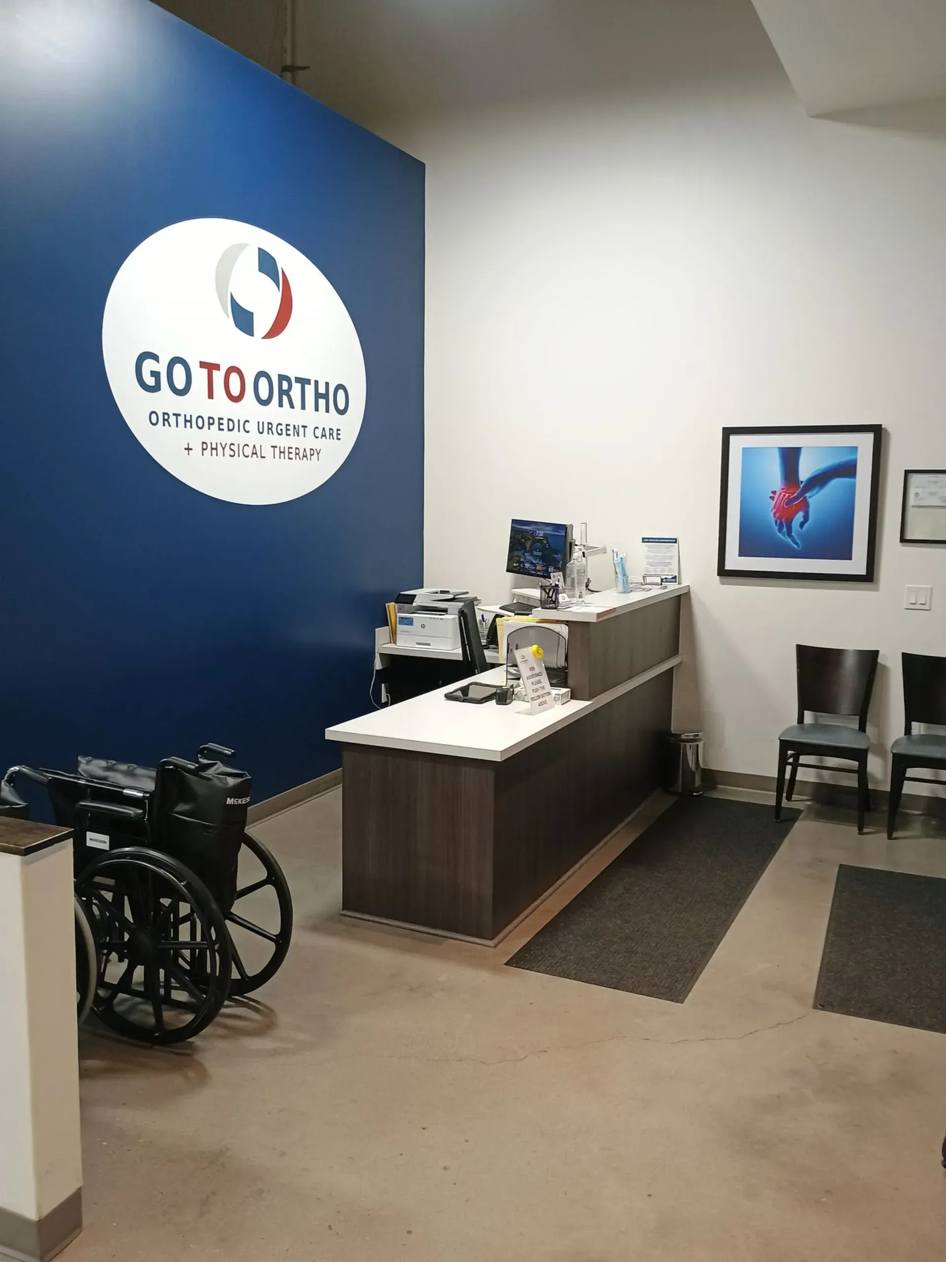 Reception area in an orthodontist's office, with a wheelchair, logo, and counter. Blue wall, neutral floor.