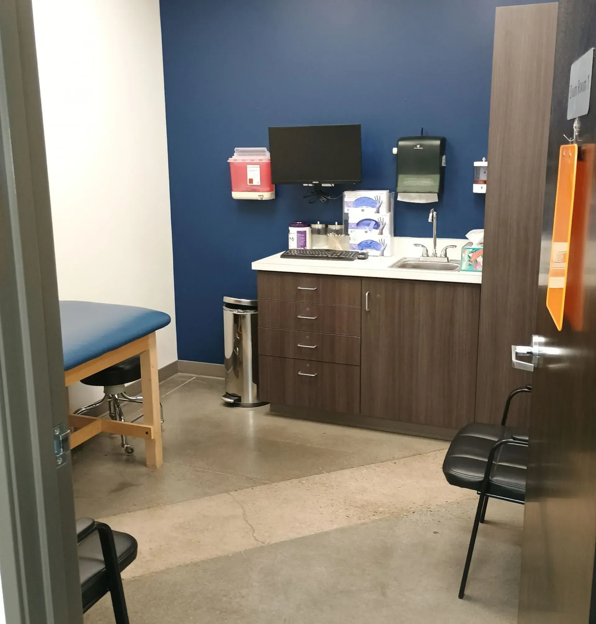 Examination room with a blue wall, medical equipment, a sink, and a patient bed.