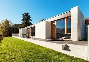 Modern house with concrete facade, large windows, and green lawn on a sunny day.