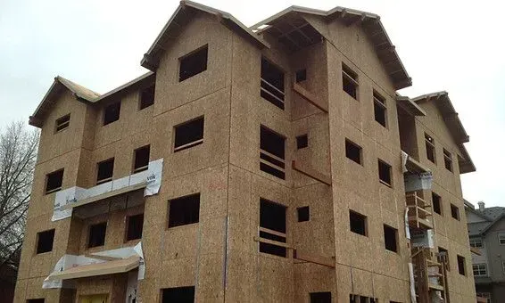 Multi-story building under construction with exposed wood sheathing and window openings.