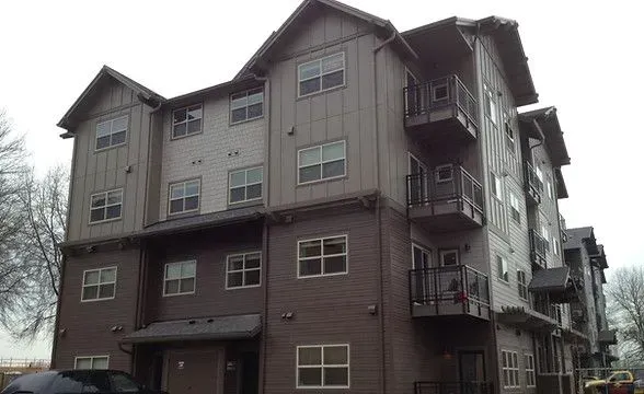 Multi-story apartment building with brown and grey siding, balconies.