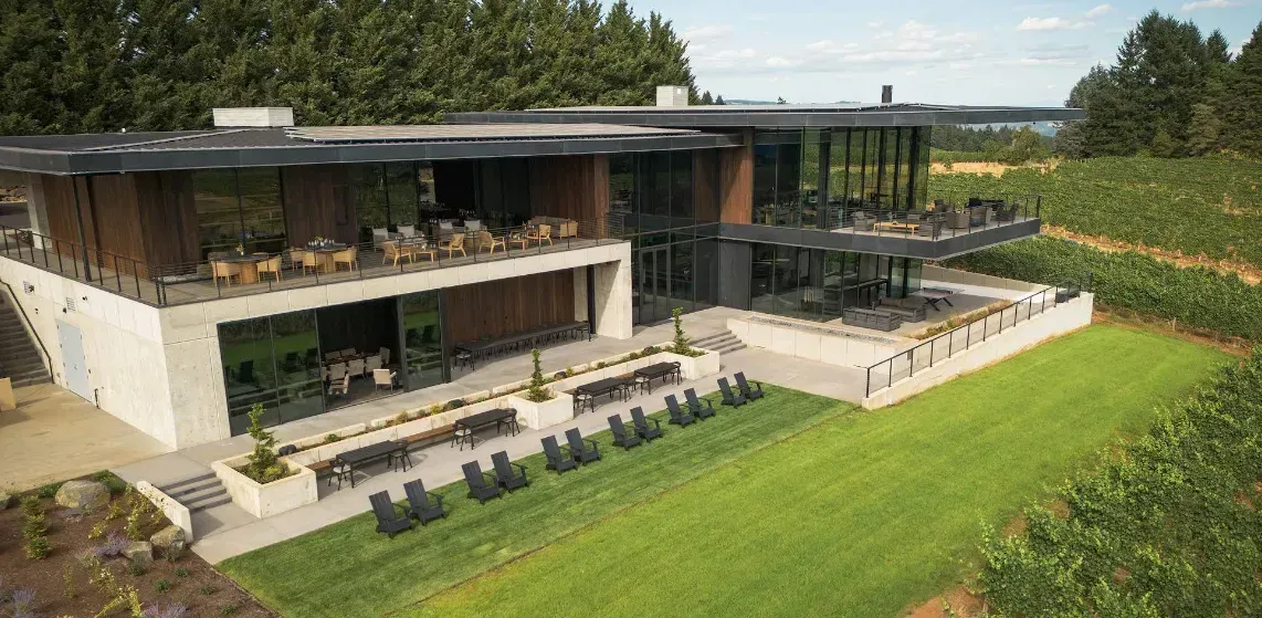 Modern building with open-air decks, set in a vineyard with green lawn and trees.
