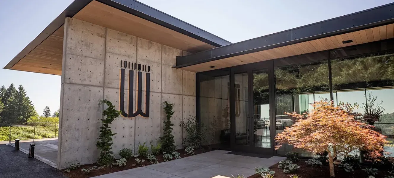 Modern building with concrete walls, glass doors, and a small tree with orange leaves.