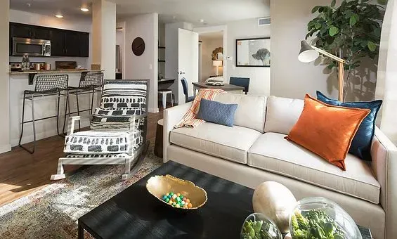 Cozy living room with cream sofa, colorful pillows, and open kitchen with bar stools.