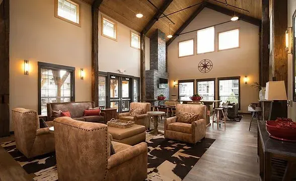 Lounge area with high ceilings, exposed beams, fireplace, leather furniture, and cowhide rug.