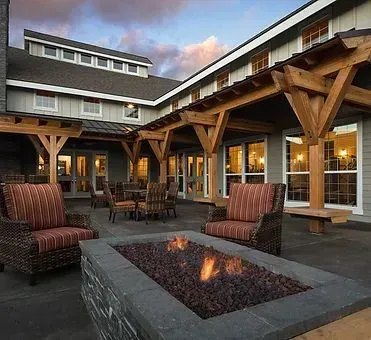 Outdoor patio with fire pit, seating, and wooden pergola. Building in the background, daytime.