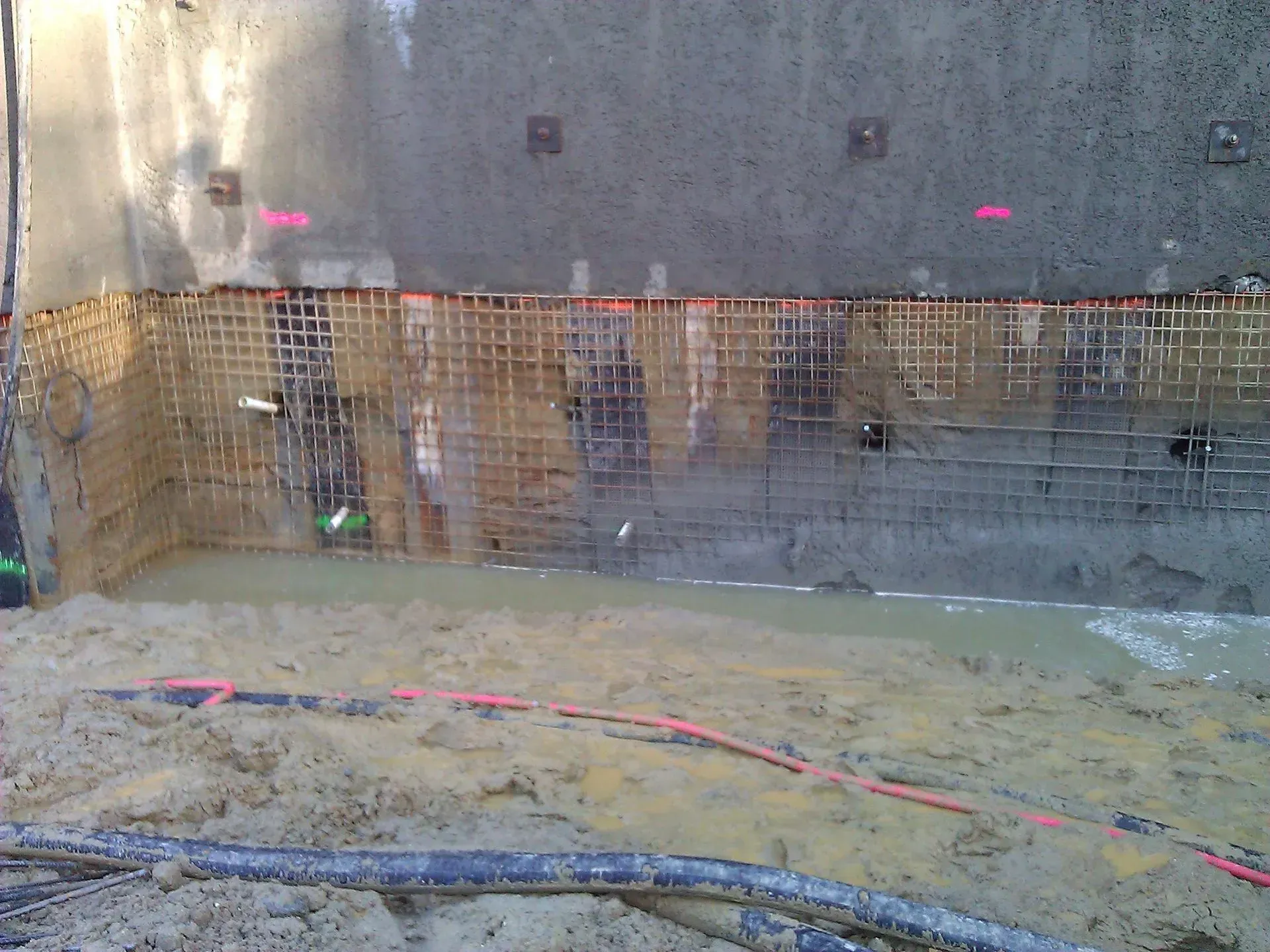 Construction site with concrete wall, rebar, and water, in an excavation.