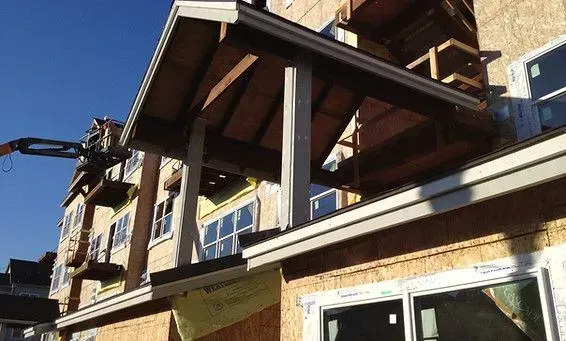 Construction of a building with wooden porch supports, and a crane in a blue sky.