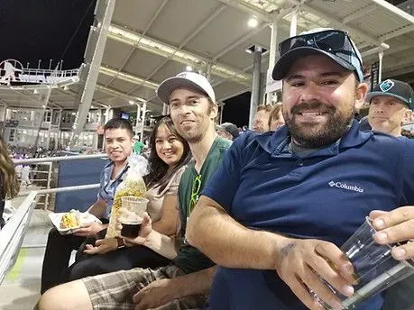 People smiling, eating, and drinking at a sports venue.