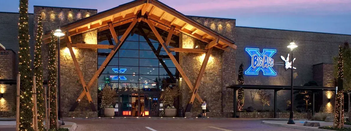 Modern, two-story house with illuminated stone and wood exterior at night. Pool and landscaped yard.