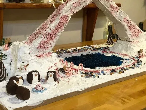 Gingerbread Arctic scene with penguins, candy canes, and blue pond, under an arch.