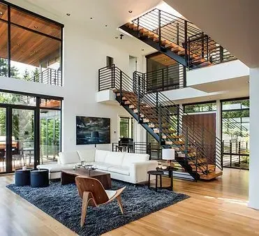 Modern living room with staircase, white walls, wood floors, large windows, and contemporary furniture.