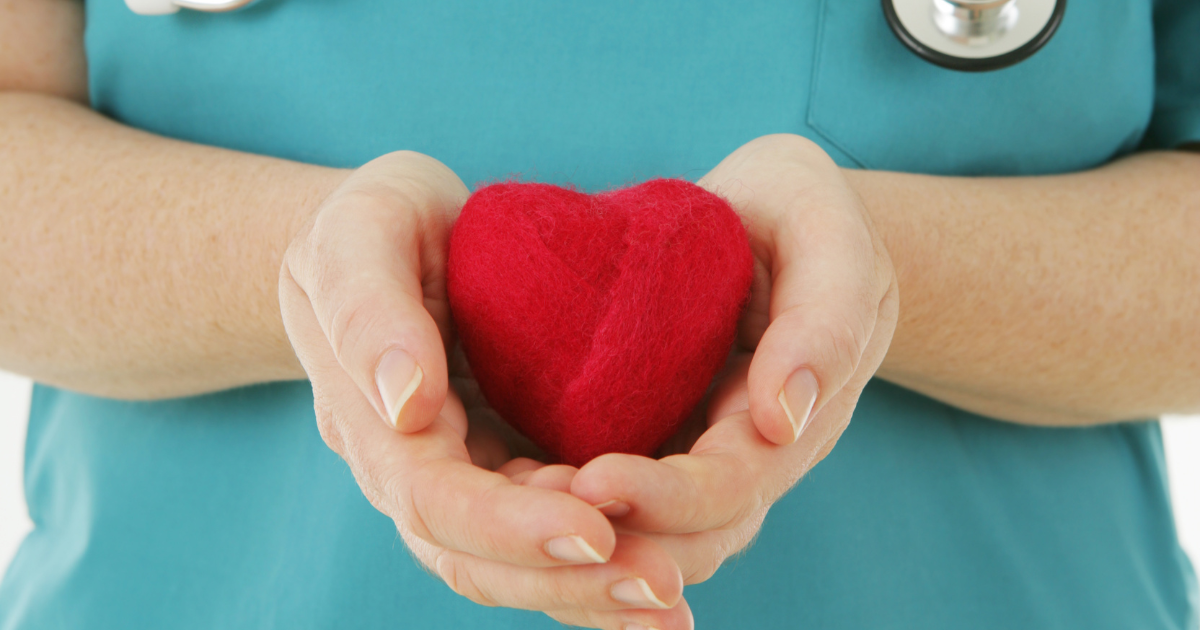 Smiling elderly woman with arm around her is comforted by a caregiver by a window.
