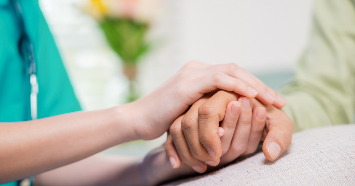 Hands clasped, one wearing a ring, held by another person in a blue sleeve; care and support.