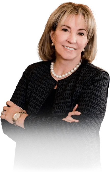 Woman in blazer with arms crossed, smiling. Wearing a pearl necklace and watch.