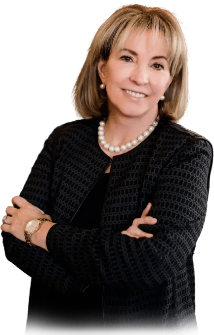 Woman with blonde hair, arms crossed, wearing a black jacket and pearl necklace, smiling.