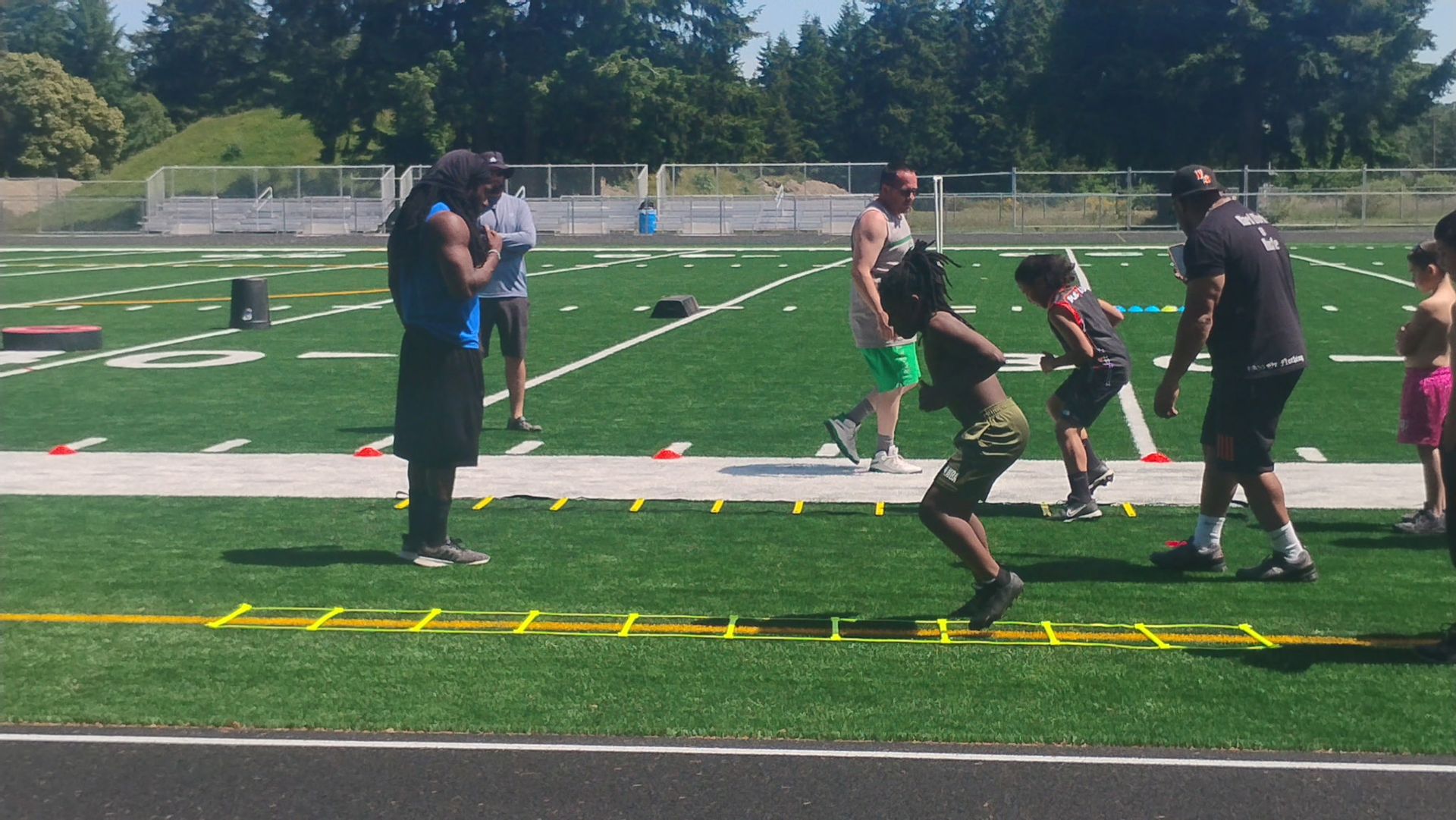 Two people in a gym holding a medicine ball. The man is wearing red shorts and the person to his left is in gray.