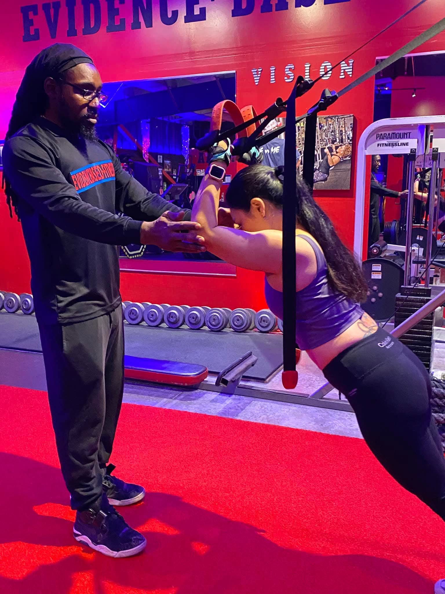 Person in gym attire lifting a barbell. Seen in mirror, lifting heavy weights, with a row of dumbbells in the foreground.