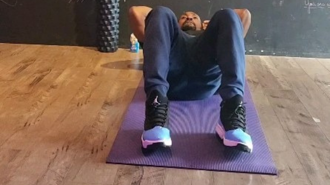 Man doing sit-ups on a purple mat, wearing blue pants and sneakers.