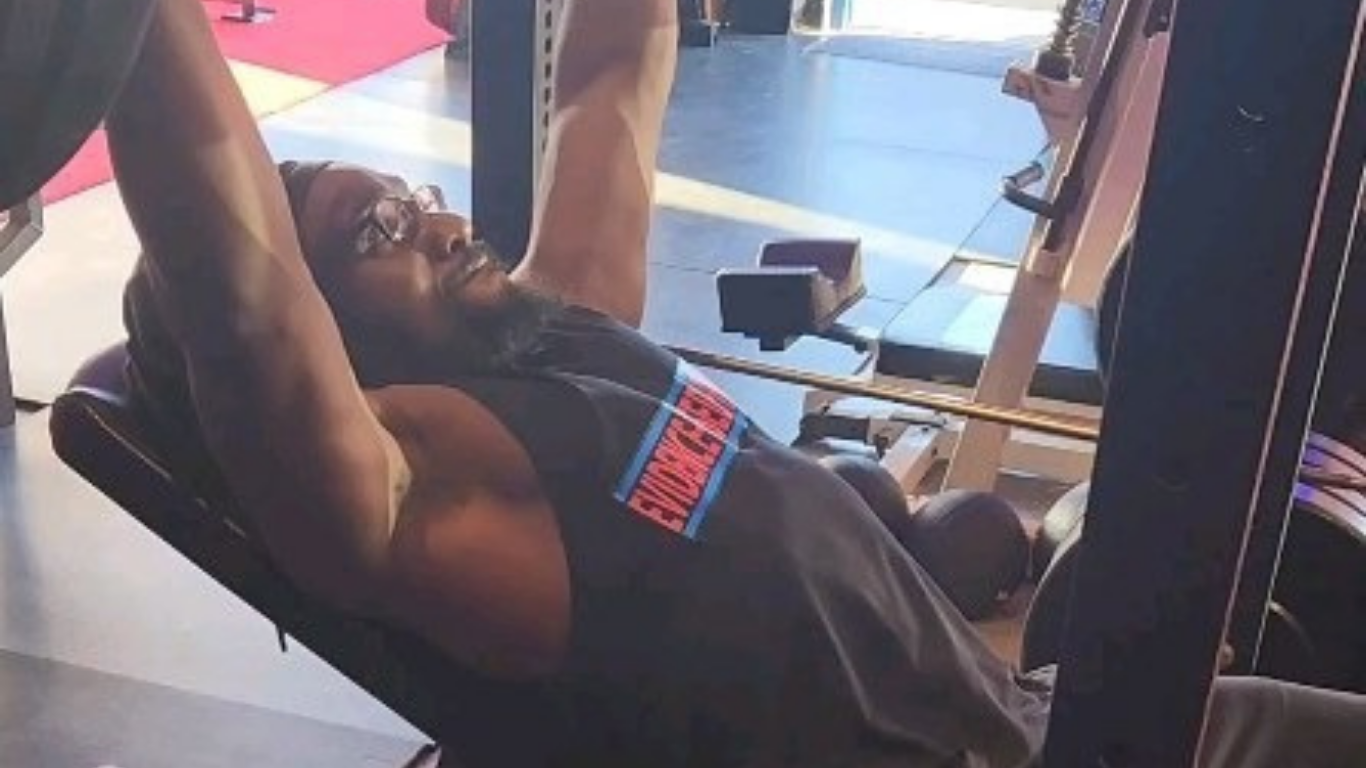 Person lifting weights on an incline bench at the gym. They are wearing glasses and a black tank top.