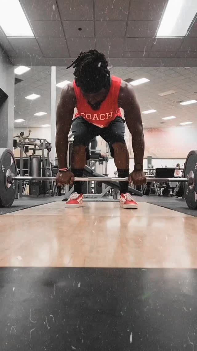A person in a gym about to deadlift a barbell on a wooden platform.