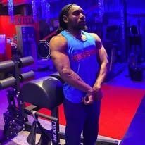 Person in a blue tank top standing in a gym, posing.