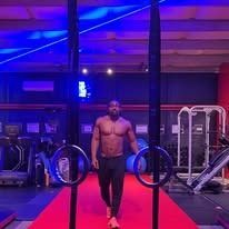 Man in gym using rings under blue and pink lights.