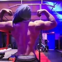 A person flexing their biceps, back view, indoors, wearing a blue head covering.