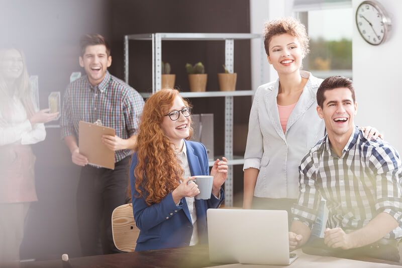 A group of people are standing around a laptop computer in an office.