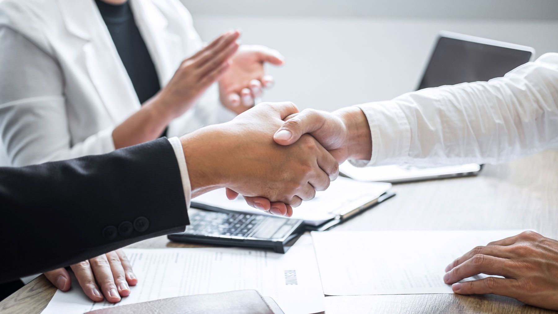 Business professionals shaking hands at a desk, representing a PEO or ASO partnership agreement