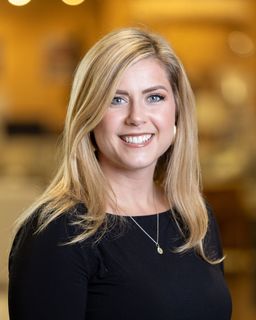 Woman with blonde hair smiles at the camera, wearing a black top and a necklace.