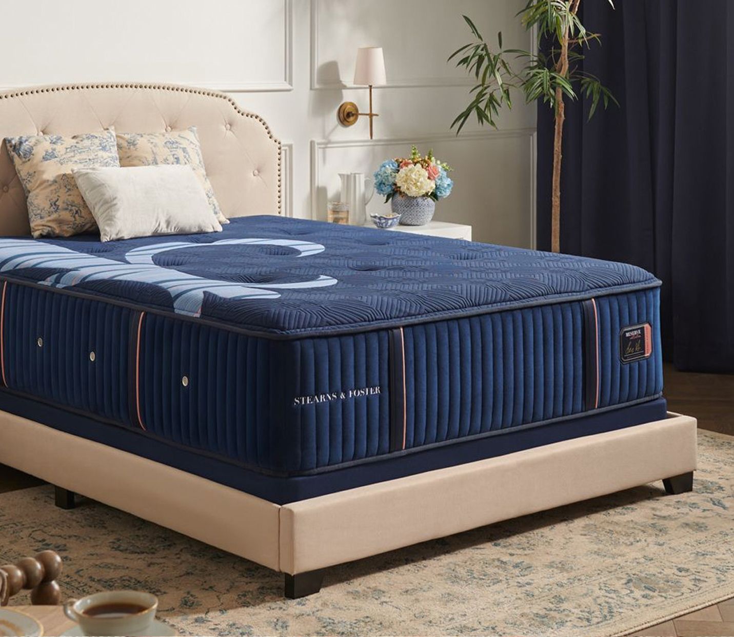 Woman with blonde hair smiles at the camera, wearing a black top and silver necklace. Blurred indoor setting.