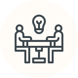 Two people at a table, brainstorming, with a lightbulb above.