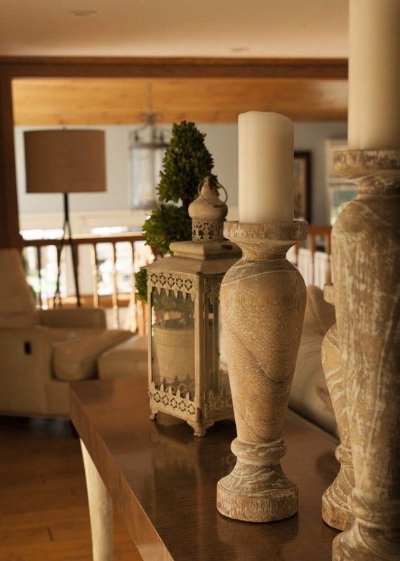 Candles and lantern on a wood table, interior setting. Cream-colored candles, neutral-toned wood.