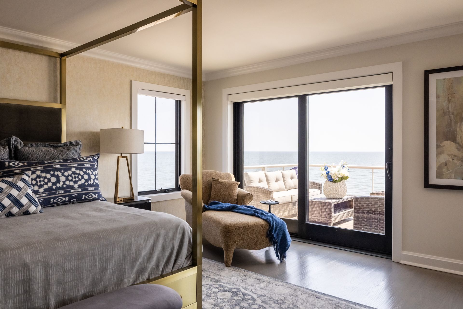 Bedroom with canopy bed, chaise lounge, and sliding glass doors overlooking a body of water.