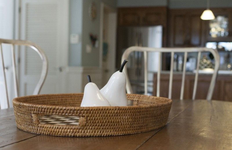 Woven tray with two white pear-shaped decorations on a wooden table, in a dining room.